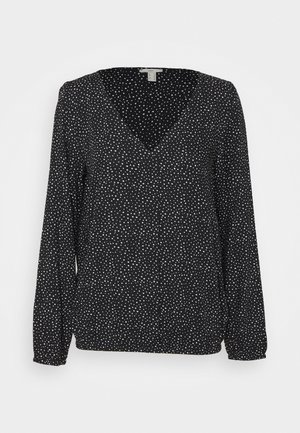 Blouse noire à manches longues avec col en V et petits pois blancs répartis uniformément sur le tissu.