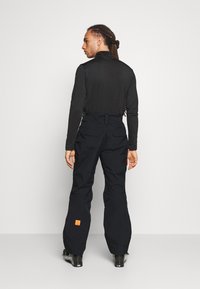Sort langærmet bluse i kombination med løse sorte bukser med et orange logo-yndlingsmærke. Glat struktur, minimalistisk design, praktisk pasform.