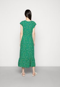 Vestido maxi floral verde com mangas curtas em camadas, parte inferior em camadas e cintura ajustada. Apresenta pequenos padrões de flores brancas e amarelas.