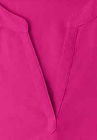 Col en tissu lisse rose vif avec un col en V profond et des coutures visibles le long des bords.