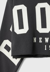 Gros plan sur un sweat-shirt noir avec de grands chiffres blancs en bloc "00", un "30" partiel, et le texte "NEW 19" imprimés sur le tissu.