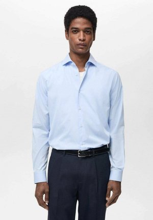 Camicia azzurra chiara a maniche lunghe con colletto classico e chiusura a bottoni, abbinata a pantaloni scuri e una cintura nera. Tessuto dalla superficie liscia.