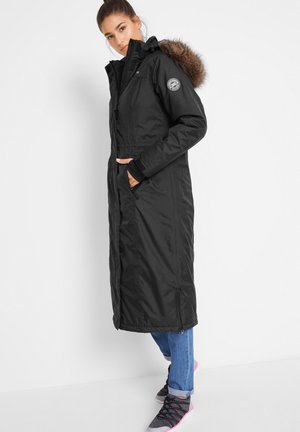 Schwarzer langer Mantel mit einem mit Fell gefütterten Kapuzen, Reißverschluss vorne und Taschen. Verfügt über eine taillierte Taille und einen gerafften Saum für einen schneidigen Look.