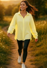 Camicetta gialla a maniche lunghe con una vestibilità comoda, realizzata in tessuto texturizzato, abbinata a leggings neri e sneakers bianche.