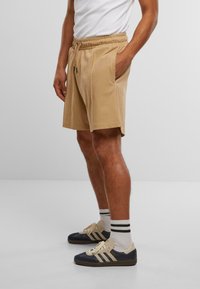 Beige bomullsshorts med elastisk midje, sidelommer og en avslappet passform, kombinert med marineblå og kremfargede sneakers samt stribede sokker.