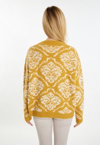 Maglione giallo lavorato a maglia con motivo floreale bianco, vestibilità rilassata, scollatura rotonda e maniche lunghe. Tessuto morbido e design leggermente over.
