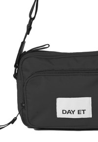 Sort nylon crossover taske med justerbar rem, der har en frontlomme med lynlås og et hvidt mærke med "DAY ET" trykt i sort.