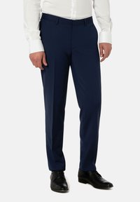 Marineblaue Anzughose mit maßgeschneiderter Passform, flacher Vorderseite und glatter Textur, kombiniert mit schwarzen Anzugschuhen. Weiße Hemdmanschetten sichtbar.