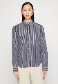 Donkerblauw-wit gestreept overhemd met knopen, een kraag, lange mouwen en knoopsluitingen. Heeft een klein logo op het linkerbovenborst.