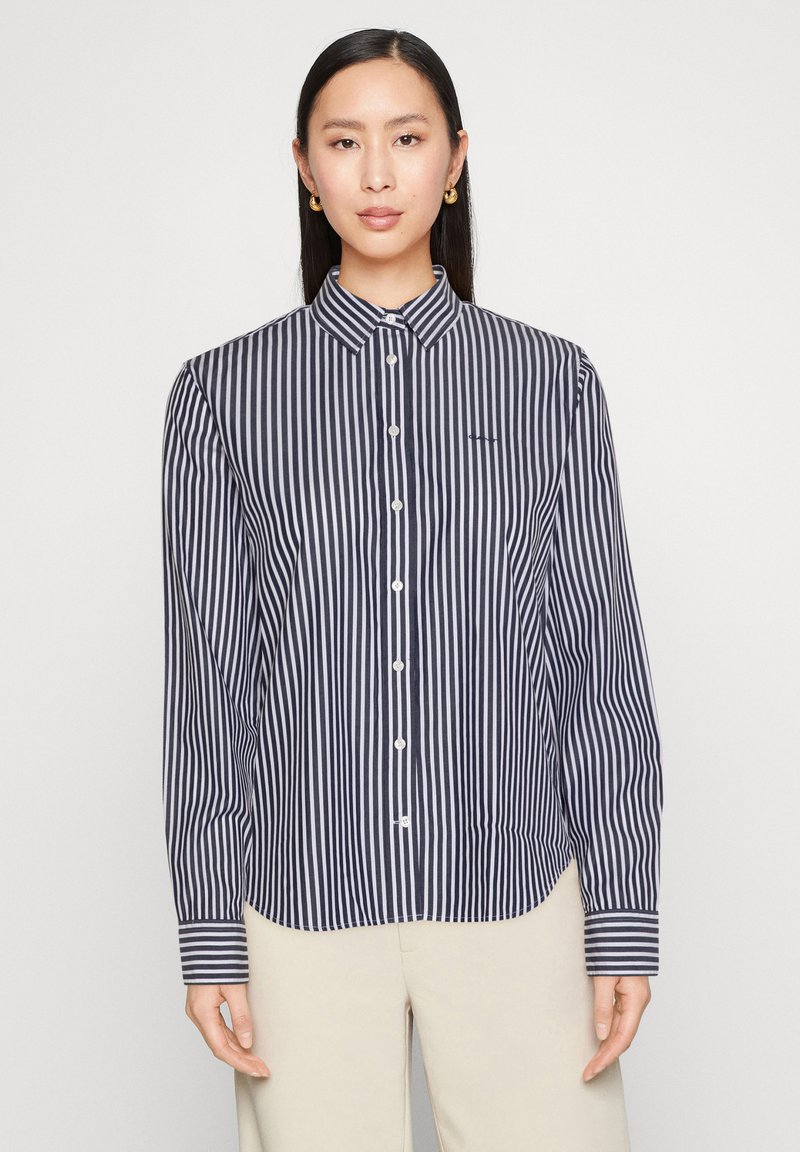 Donkerblauw-wit gestreept overhemd met knopen, een kraag, lange mouwen en knoopsluitingen. Heeft een klein logo op het linkerbovenborst.