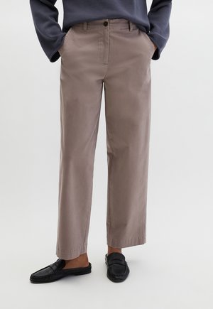 Pantalon marron clair à coupe décontractée, doté de poches latérales, d'une fermeture à boutons à l'avant et d'un tissu lisse. Associé à des chaussures noires à enfiler.