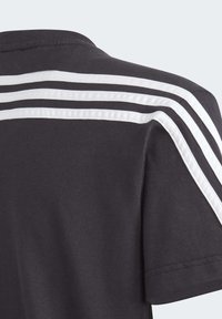 Camiseta negra de cuello redondo, hecha de algodón, con tres rayas verticales blancas a lo largo de los hombros.