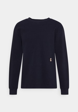 Czarny sweter z długim rękawem i okrągłym dekoltem, z prążkowanymi mankietami oraz małym złotym emblematem "C" na dole po prawej stronie z przodu.