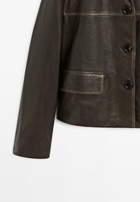 Tmavě hnědá kožená bunda se zapínáním na knoflíky a kapsou na klopě, vystavená na bílém pozadí.