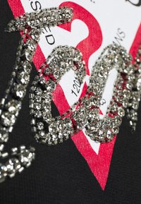 Tessuto nero con una grafica rossa e bianca, arricchita da accenti di strass che formano un motivo prominente. Texture lucida con un design audace.