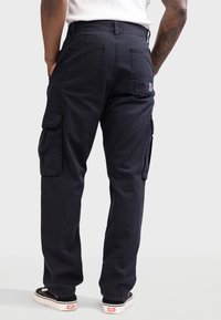 Schwarze Cargo-Hosen aus einem Baumwollmix, mit Seitentaschen, zwei Gesäßtaschen und einem lockeren Schnitt. Mit sichtbaren Nähten akzentuiert.