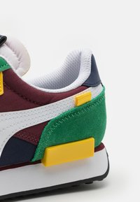 Sneaker dengan desain berwarna-warni yang menampilkan bahan burgundi, hijau, navy, dan putih. Aksen tekstur dan detail klip tumit kuning.