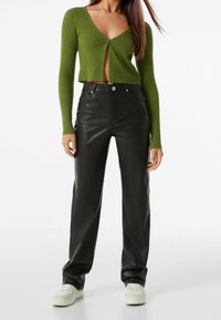 Cardigan cropped a coste verde con chiusura a bottoni, abbinato a pantaloni in pelle nera a vita alta e sneaker chiare.