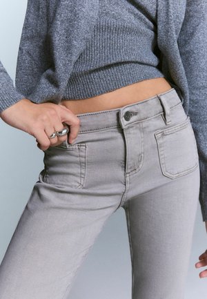 Hellgraue Jeans im Slim-Fit mit klassischem Fünf-Taschen-Design und subtilen Nähten. Kombiniert mit einem strukturierten grauen Pullover.