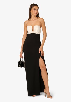 Schwarzes trägerloses Kleid mit einem cremefarbenen Oberteil, tiefem V-Ausschnitt und einem hohen Schlitz bis zum Oberschenkel. Glattes Material mit einer figurbetonten Silhouette, kombiniert mit einer schwarzen Handtasche.