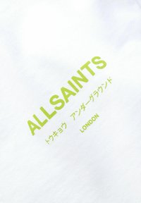 Balts audums T-krekls ar lieliem zaļiem "ALLSAINTS" uzrakstiem un mazākiem japāņu rakstzīmēm. Vienkārša dizaina, mīksta tekstūra un ikdienišķs stils.