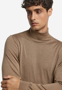 Brauner Rollkragenpullover mit langen Ärmeln, aus weichem Stoff. Hat ein tailliertes Design und einen gerippten Kragen; minimale Textur.