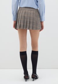 Braunes kariertes, gefaltetes Miniröckchen mit hohem Taillenbund, kombiniert mit kniehohen schwarzen Socken und schwarzen, verzierten Absatzschuhen.