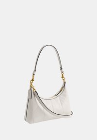 Sac à main blanc matelassé avec des finitions dorées, deux poignées dont une bandoulière, et une petite étiquette rectangulaire attachée près du haut.