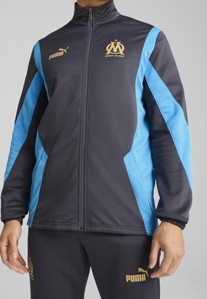 Mørkegrå sportsjakke med lyseblå sideaccenter, lynlåse foran, høj krave og gyldne logoer. Blødt, struktureret stof.