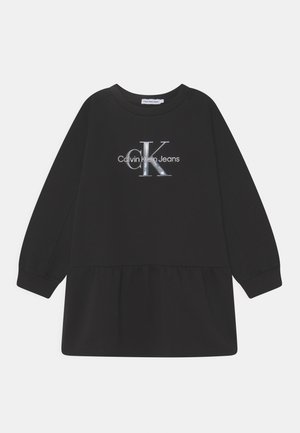 Czarna sukienka z długim rękawem, falbanowym dołem i srebrnym logo "Calvin Klein Jeans" umieszczonym na środku klatki piersiowej.