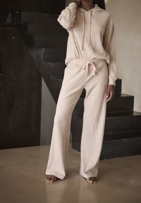 Beżowy dres z prążkowanego materiału składający się z bluzy z kapturem i długimi rękawami oraz spodni z gumką w pasie, wykonany z fakturowanej tkaniny o luźnym kroju.