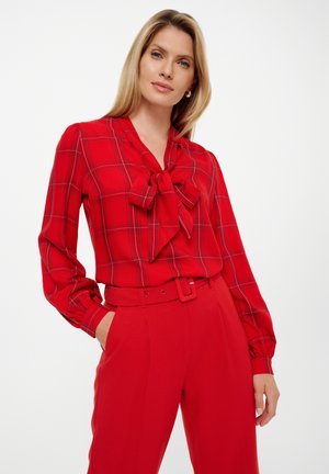 Rood geruite blouse met een strikje bij de kraag, lange mouwen en een relaxed fit, gedragen met rode hoog-getailleerde broeken.