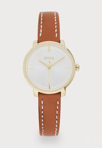 Reloj de tono dorado con una esfera blanca. La correa de piel marrón presenta costuras blancas. Caja redonda sencilla y marcadores de horas minimalistas.