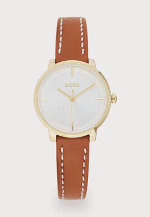 Montre dorée avec un cadran blanc. Le bracelet en cuir marron présente des coutures blanches. Boîtier rond simple et marqueurs d'heure minimalistes.