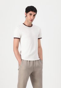 White short-sleeve t-shirt with a brown ribbed collar and sleeve accents, fitted design, displayed with light beige loose-fitting pants.