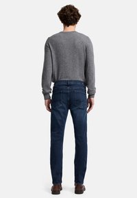Grauer Pullover, blaue Jeans, Rückansicht. Der Pullover hat einen runden Ausschnitt und lange Ärmel; die Jeans haben eine Slim-Fit-Passform mit Gesäßtaschen. Braune Schuhe sind sichtbar.