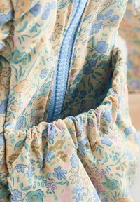 Floral-patterned fabric bag with pastel tones. Features a light blue zipper and gathered accents. The material appears smooth and lightweight.