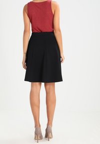 Svart plisserad kjol med hög midja, kombinerad med en röd ärmlös topp. Bruna, strukturerade klackskor fulländar looken.