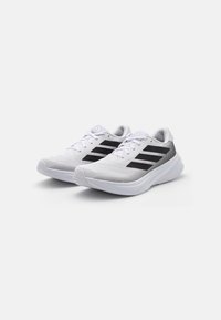 Chaussures de sport blanches avec accents noirs, en tissu en maille, semelle rembourrée et lacets plats. Elles présentent trois bandes noires sur les côtés.