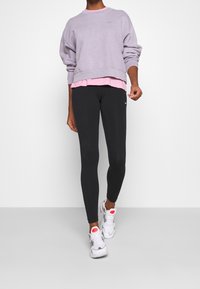 Grå oversized sweatshirt ovanpå en rosa T-shirt, tillsammans med svarta leggings och vita träningsskor med rosa accenter.