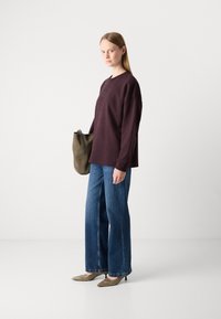 Sudadera oversized color marrón, vaqueros de pierna recta azules, bolso de tela color oliva y zapatos de tacón beige. Tejido suave y corte relajado.