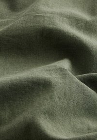 Olivově zelená látka s jemným, texturovaným povrchem, ukazující přírodní vlákna a drobné barevné variace, slabě pomačkaná.