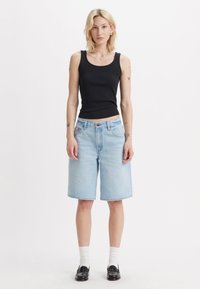 Črn rebrast top s zaobljenim izrezom, v kombinaciji z svetlo modrimi denim bermuda kratkimi hlačami. Model nosi bele nogavice in črne loafer čevlje.