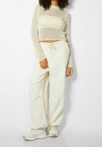 Stickad, långärmad, ljusgul topp med öppen meshstruktur; kombinerad med vida, krämfärgade byxor med elastisk midja och dragsko.