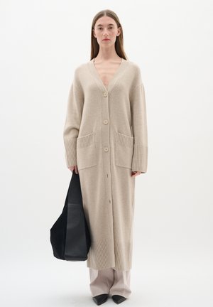 Beige lange cardigan van zachte breigoed met een V-hals, vijf knopen, geribde manchetten, twee voorzakken en zijsplitten.