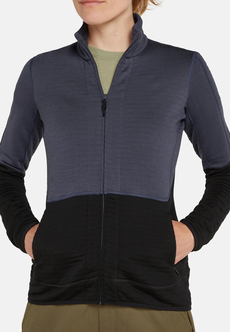 Chaqueta de forro polar con cierre frontal, con un diseño en bloques de color en gris oscuro y negro, mangas largas y bolsillos laterales. Textura elástica.