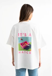 Biała bawełniana koszulka T-shirt z kolorową grafiką na plecach z motywem tenisa, napisem "TO JEST MISTRZOSTWO" i pudełkiem z piłkami do tenisa.