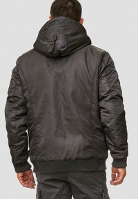 Svart vadderad jacka med huva, ribbade ärmslut och midja. Tyget verkar slätt med en lätt glans och har sydda detaljer på baksidan.