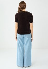 Brauner Pullover mit kurzen Ärmeln, strukturierter Oberfläche und dekorativem, mit Perlen besetztem Rundhalsausschnitt, kombiniert mit hellblauen Jeans mit weitem Bein.