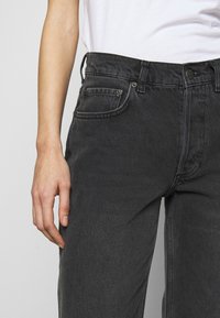 Jeans de mezclilla gris oscuro con un ajuste holgado, que cuentan con bolsillos estándar, un botón funcional y una tela ligeramente texturizada.